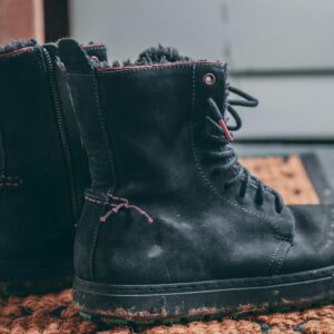 Close-up view of black leather winter hiking boots on a doormat indoors.